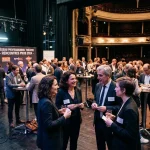 Groupe de professionnels en tenue formelle échangeant autour de verres lors d’un événement de théâtre, sur scène et dans les coulisses. Troupe de théâtre professionnelle.
