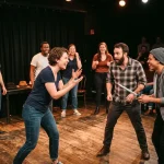Trois improvisateurs jouent une scène sur scène, entourés d’un public qui rit et applaudit. Le groupe discute avec énergie, un baton d’accessoire à la main et les spectateurs en arrière-plan. application improvisation théâtre